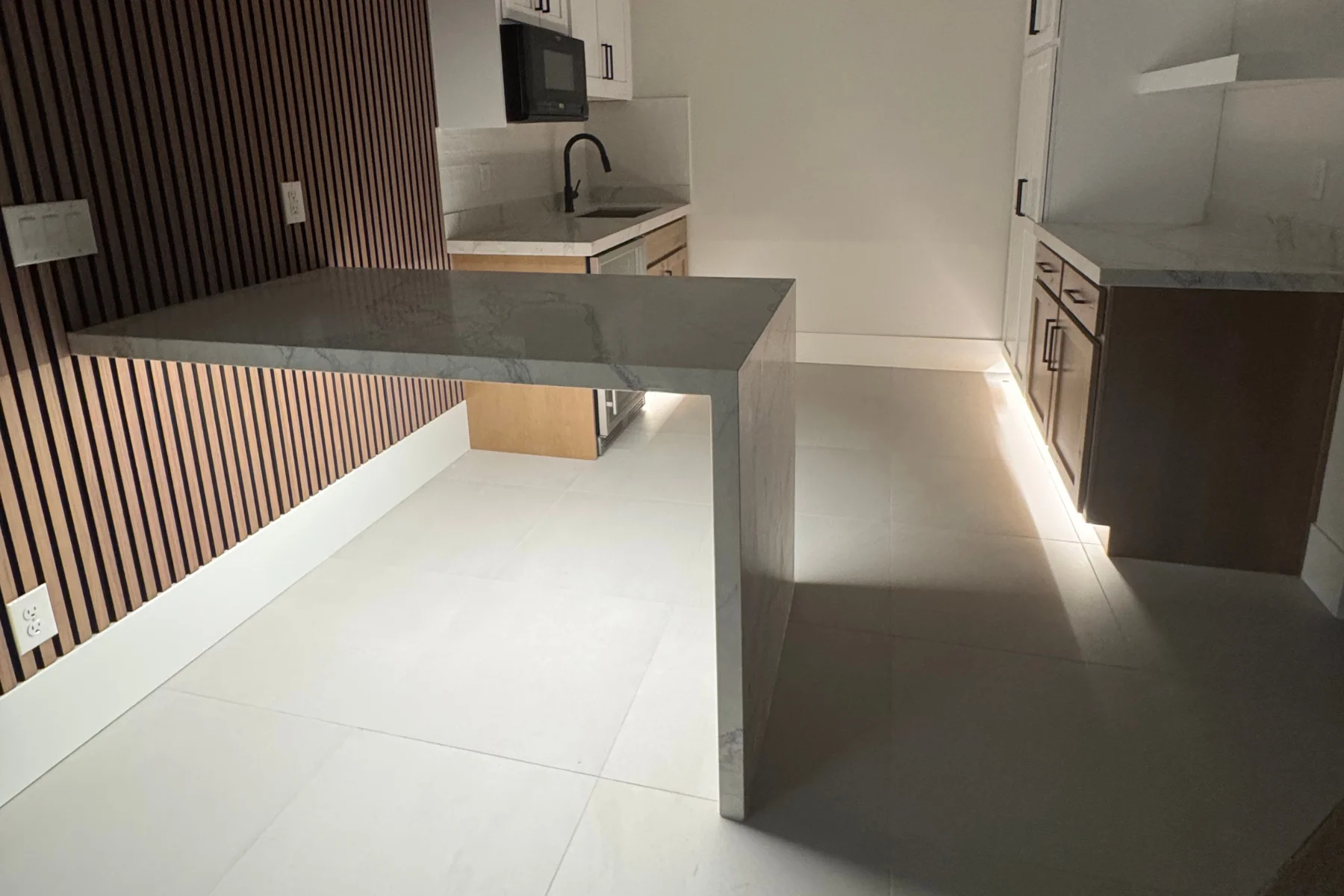 LED cabinet and toe-kick accent lighting illuminating a kitchen floor beside a waterfall countertop