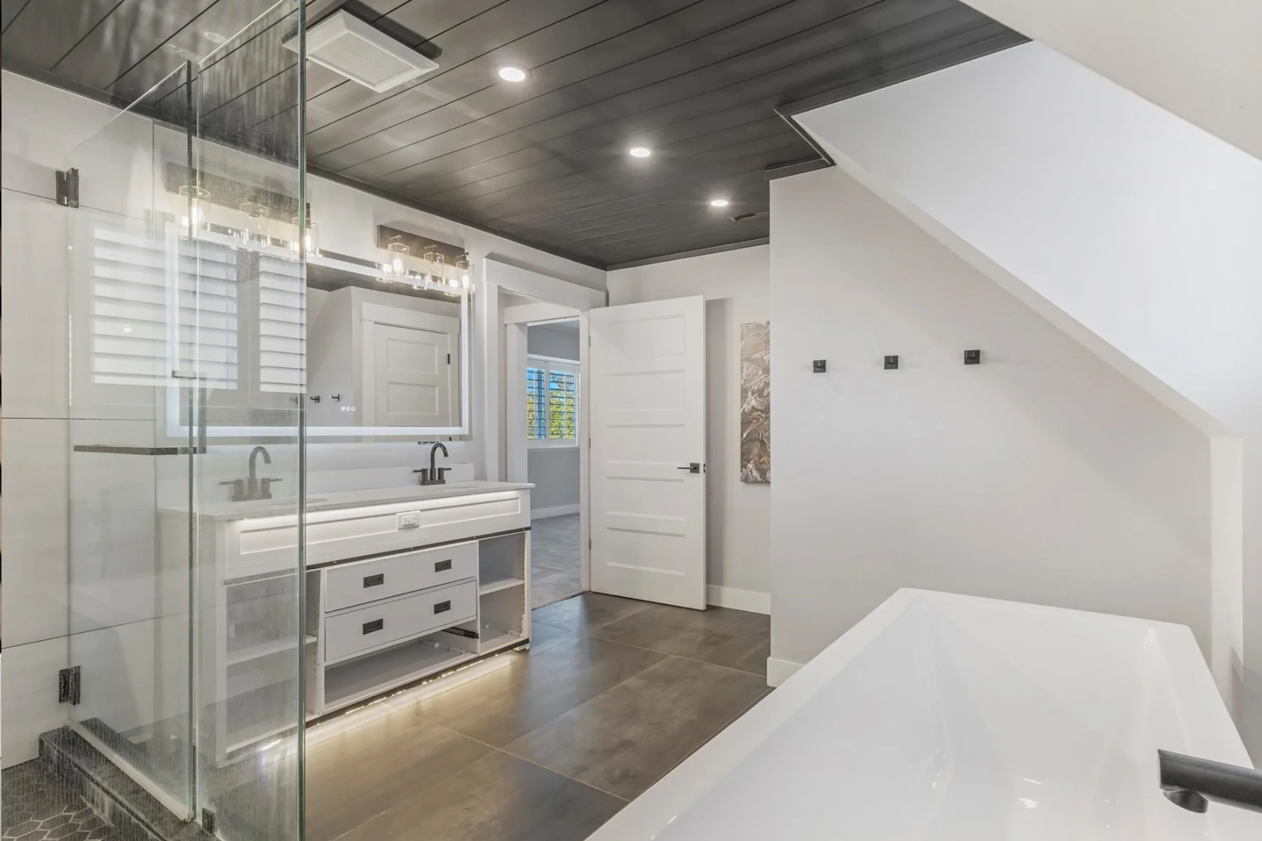 Bathroom vanity accent lighting beneath floating cabinets with recessed ceiling lights and a freestanding bathtub